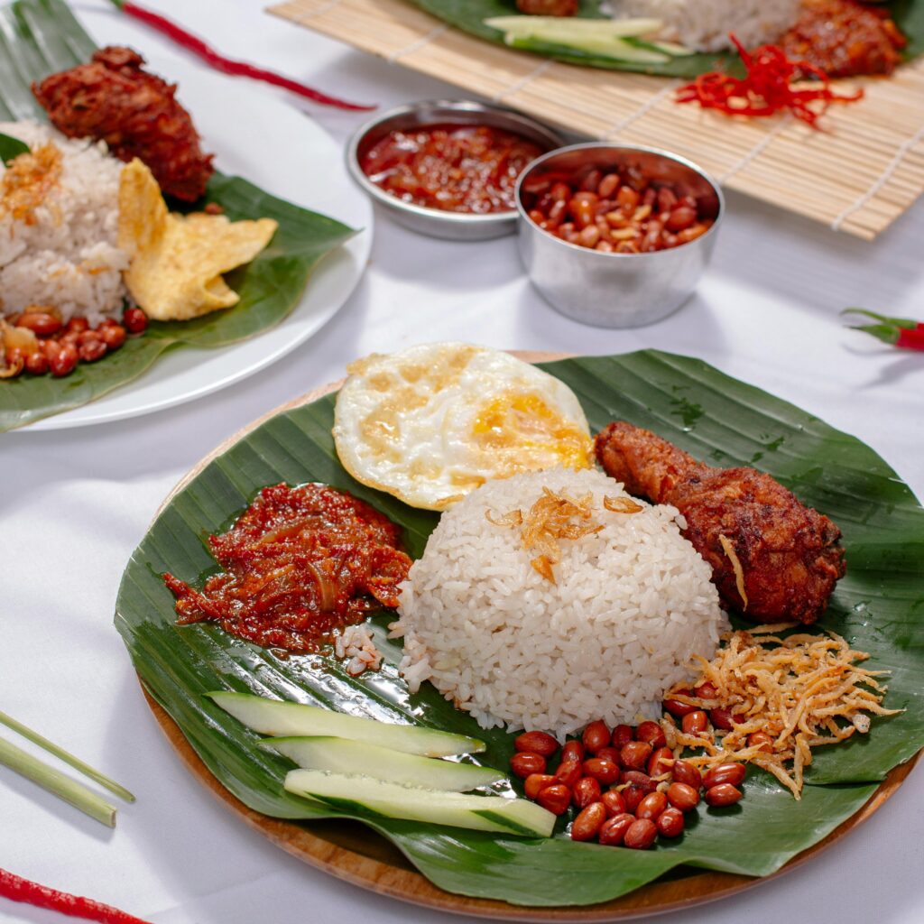A delicious Nasi Lemak dish with rice, fried chicken, sambal, and garnishes served on banana leaf.