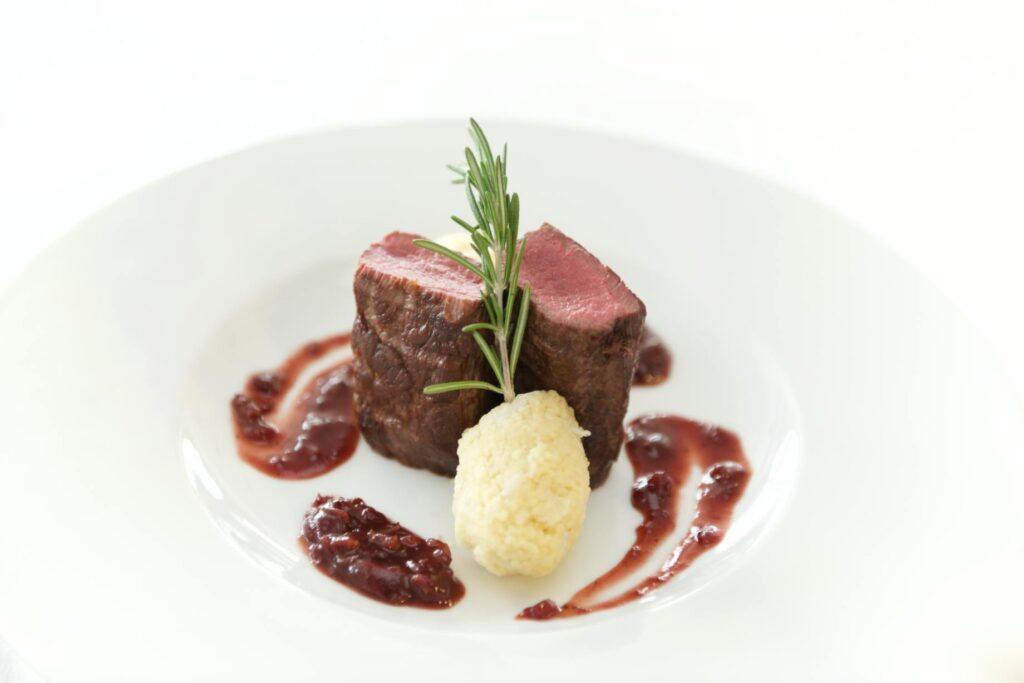 Elegant beef steak with rosemary and sauce on a white plate.