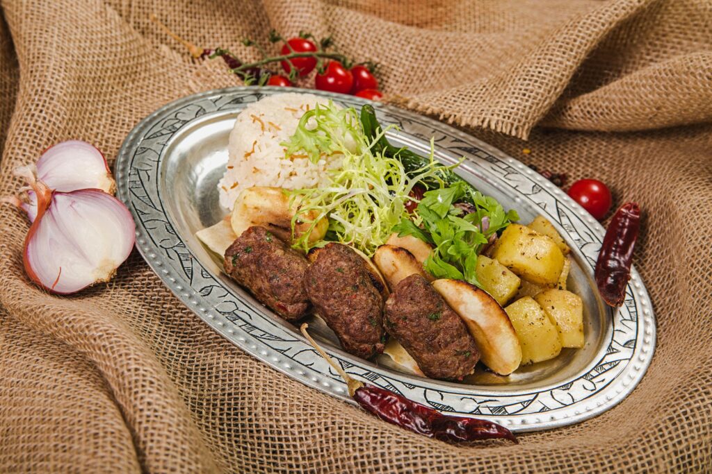 An appetizing Mediterranean dish featuring grilled meat, rice, potatoes, and fresh salad on a decorative platter.